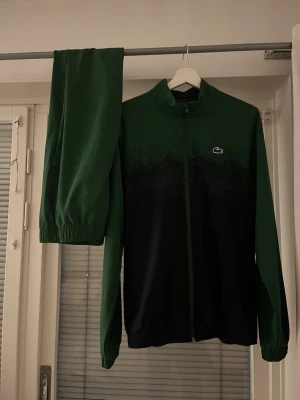 Grön träningsdress från Lacoste - Snygg grön träningsdress från Lacoste med dragkedja på jackan. Jätte rent använt och sitter M/L