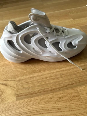 Vita Adidas sneakers med futuristisk look - Sneakers i vitt med futuristisk design och utskurna detaljer i ovandelen. Skon har chunky sula, meshpartier och hög vadderad plös. Materialet är en mix av textil och syntet. Perfekt för dig som gillar statement-skor och modern stil.