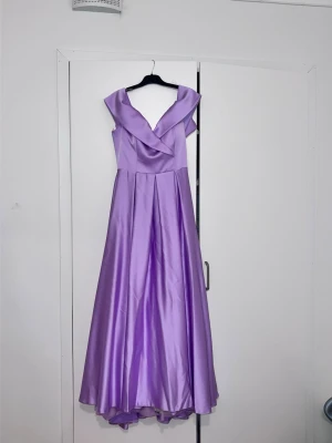 Lång lila balklänning i satin 💜 - Säljer en fantastisk och helt oanvänd klänning i en vacker ljuslila färg. Klänningen är köpt hos Queen i Norrköping och är endast provad.  ✨ Detaljer:  * Passar storlek 36–38 * Avtagbart strassbälte ingår * Klänningen är insydd till nuvarande storlek (36–38), men sömmarna kan enkelt sprättas upp hos en skräddare så att den blir större igen. * Mycket elegant modell med fin drapering över bysten och vackert fall.