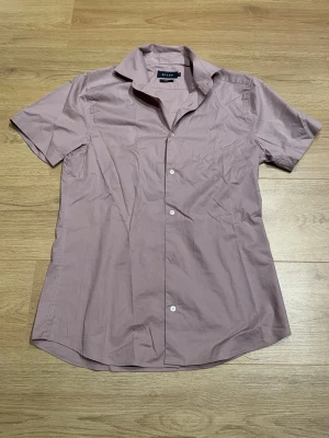 Ljuslila kortärmad skjorta - Kortärmad skjorta i ljuslila bomull med klassisk krage och knappar framtill. Skjortan har en enkel och stilren design som passar perfekt till jeans eller chinos. Perfekt för dig som gillar en clean och avslappnad look.