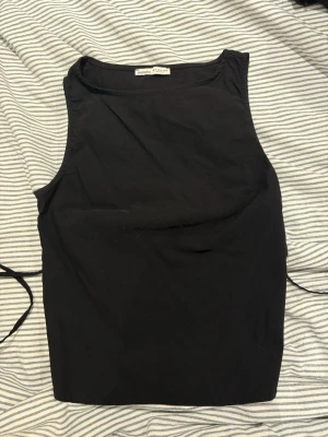 Svart ärmlös linnetopp med knyt - Säljer en svart, ärmlös linnetopp med rund halsringning och knytband i ryggen. Toppen har en clean och enkel design som passar perfekt till jeans eller kjol. Materialet känns mjukt och lätt, perfekt för varmare dagar.