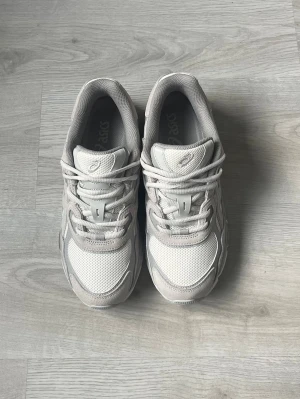 Gråa Asics sneakers mesh och mocka - Säljer ett par stilrena sneakers från Asics i ljusgrått. Skorna har en kombination av mesh och mocka, med klassiska Asics-detaljer på sidorna. Sulan är vit och grå, och designen är chunky och sportig. Perfekta för en trendig och avslappnad look. Pris kan diskuteras 