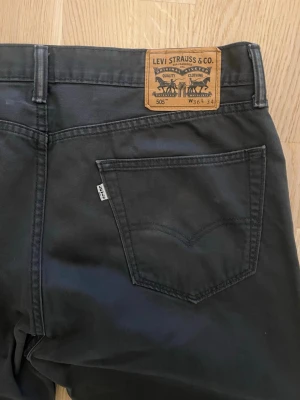 Svarta Levi's 505 jeans - Säljer ett par svarta Levi's 505 jeans med klassisk femficksdesign och läderpatch bak i midjan. Jeansen har raka ben och är tillverkade i bomull för en skön och slitstark känsla. Perfekta till vardags och passar till det mesta.