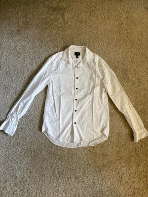 H&M Slim Fit skjorta - Vit skjorta från H&M i slim fit med snygga mörka knappar och diskreta detaljer i kragen. Sparsamt använd och i fint skick.  Perfekt till kostym, chinos eller jeans.  📦 Snabb leverans! Hör gärna av dig!