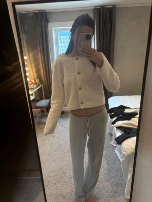 Mysig loungewear-set i vitt och grått - Säljer ett mysigt loungewear-set med en fluffig, vit kofta med träknappar och rund hals samt ett par grå mjuka byxor med dragsko i midjan. Perfekt för chill dagar hemma och riktigt bekvämt material.