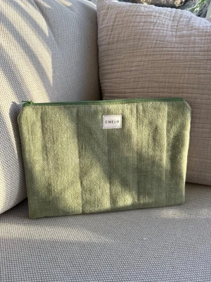 Grön tygnecessär/fodral medium från Emelo - Snygg grön necessär i tyg från Emelo med dragkedja upptill. Perfekt för att förvara småprylar, smink eller pennor. Passar även för iPad. Enkel och stilren design med en liten vit logotyp på framsidan. Passar lika bra i väskan som på skrivbordet. Mått ca 29x20cm