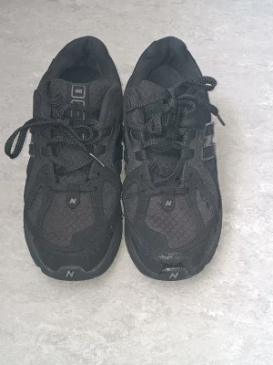 Svarta New Balance sneakers - Snygga helsvarta sneakers från New Balance med mesh och mockadetaljer. Skorna har klassisk snörning, låg profil och diskret logga på sidan och tungan. Perfekta för dig som gillar stilrena och sportiga skor.