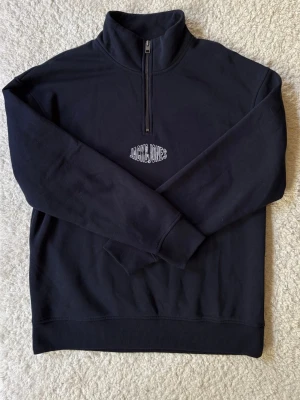 Mörkblå halfzip hoodie Jack & Jones - Mörkblå hoodie från Jack & Jones med halv dragkedja och hög krage. Broderad logga på bröstet i vitt. Tillverkad i mjukt sweatshirtmaterial och har ribbade muddar vid ärmslut och nederkant. Perfekt för en avslappnad och stilren look.