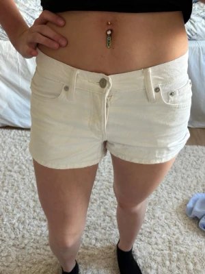 Vita midwaist shorts i bomull - Snygga vita shorts med midwaist passform och klassisk femficksdesign. Tillverkade i mjuk bomull med bälteshällor och knappstängning framtill. Perfekta för varma dagar och enkla att matcha med olika toppar.