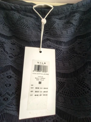 Marinblå spetsklänning från Vila - Snygg marinblå kortklänning från Vila i spets med offshoulder-design. Klänningen har ett vackert spetsmönster och är fodrad undertill. Perfekt för dig som vill ha en elegant och stilren look.