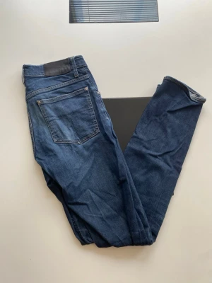Mörkblå raka jeans herr - Snygga mörkblå jeans med rak passform och klassisk femficksdesign. Jeansen har normal midja, bälteshällor och silverfärgade nitar. Tillverkade i denim med en lätt tvättad look för en avslappnad stil.