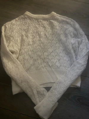 Vit spetsstickad tröja från H&M - Supersöt vit stickad tröja från H&M med spetsliknande mönster och ribbade muddar. Tröjan har rund halsringning och lång ärm, perfekt för lager på lager. 