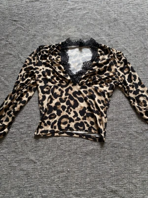 Leopardmönstrad topp med spets - Snygg leopardmönstrad topp med lång ärm och v-ringning dekorerad med svart spets. Toppens material känns mjukt och stretchigt. Den är croppad och har ”puffiga” ärmar.