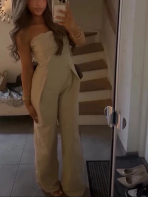 Beige jumpsuit - Snygg beige axelbandslös jumpsuit med vida ben och markerad midja. Jumpsuiten har en elegant, figurnära överdel och är tillverkad i ett mjukt tyg🤍 passar storlek S-M