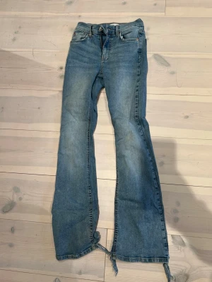 Blå bootcut jeans  - Säljer ett par blå bootcut jeans i storlek 34. Jeansen har råa, fransiga benslut och klassisk femficksdesign. De är tillverkade i denim och har en snygg, lätt tvättad look. Perfekta för dig som gillar en avslappnad och trendig stil.