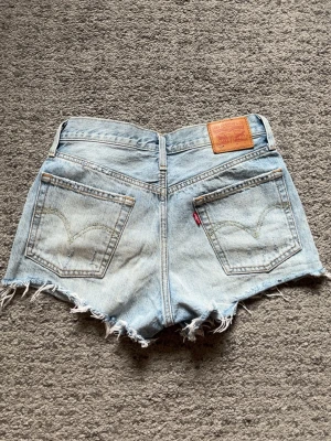 Levi's jeansshorts - Ljusblå jeansshorts från Levi's med fransade kanter och klassiska bakfickor. W27 men skulle säga att den passar en XS. Jättefin passform och perfekt för sommaren☀️ 