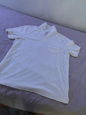 Vit henley från H&M i bomull - Klassisk vit henley från H&M i mjuk bomull. Skjortan har korta ärmar, bröstficka och en avslappnad krage. Perfekt för en clean och enkel stil.