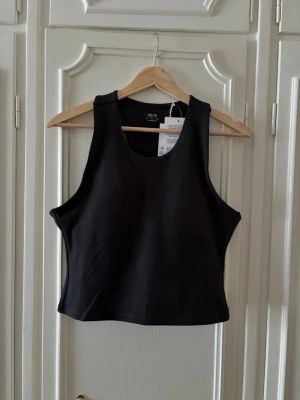 Svart topp från Asos  - Snygg svart linnetopp från 4505 med inbyggd bh. Toppen har en croppad passform och är tillverkad i ett stretchigt material som passar perfekt till träning eller som ett stilrent basplagg. Helt oanvänd med alla lappar kvar! Nypris är 289 kr. 