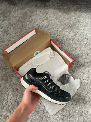 Nike p6000 svart - Snygga svarta sneakers med vit sula och detaljer i vitt och silver. Skon har en sportig design med mesh och syntetmaterial, samt tydliga paneler och snörning. Perfekt för dig som gillar streetwear och vill ha en modern look.