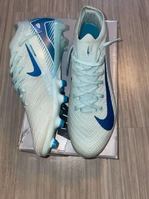 Nike ljusblå fotbollsskor med blå sula - Nike Mercurial Vapor 16 Elite storlek 44, Helt nya och aldrig använda, säljer för att dom var för stora för mig, köptes i 2024 när dom kom ut men är i behov av pengar för ett par nya fotbollsskor, skorna säljs inte längre, box och stringbag medföljer.        Skriv vid frågor!!!