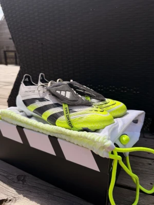 Adidas Predator lime fotbollsskor strl 42,5 - Snygga Adidas Predator fotbollsskor i vitt, svart och limegrönt med klassiska tre ränder på sidan. Skorna har snörning, låg profil och greppvänlig sula för bästa kontroll på planen. Materialet är syntet och textil, perfekt för snabba vändningar och bra bollkänsla. 