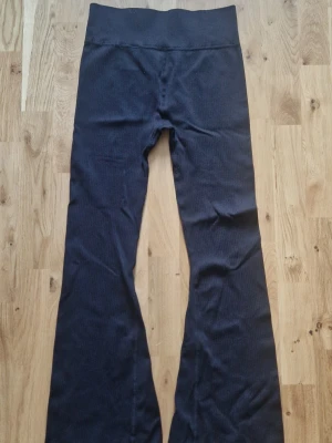 Bootcut leggings - Säljer ett par svarta ribbade leggings med bootcut-ben och hög midja. Materialet är stretchigt och mjukt, perfekt för en avslappnad och trendig look. Passar dig som gillar bekväma men ändå snygga byxor.