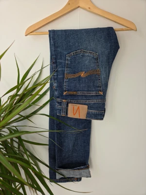 Nudie Jeans - Säljer ett par klassiska blå jeans från Nudie Jeans med snygga slitningar och kontrastsömmar. Jeansen har fem fickor, normal midja och raka ben. Tillverkade i slitstark denim med Nudie-logga på bakfickan. Storlek W 30. L 32. Model. Long John. 