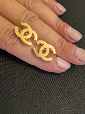 Guldfärgade örhängenmed CC-logga - Snygg guldfärgade örhängenmed dubbla C-loggor i metall. Ringen har en modern och trendig design som sticker ut och passar perfekt för dig som gillar statement-smycken. Enkel att matcha med andra accessoarer.