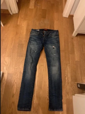 Mörkblå slim jeans från Jack & Jones storlek 29/32 - Mörkblå slim fit jeans från Jack & Jones, modell Slim Glenn. Jeansen har slitna detaljer och lätt tvättade partier för en cool look. Klassisk femficksmodell med dragkedja och knapp. Perfekta för dig som gillar en smalare passform. Kolla sista bild för jeans lappen som är sliten. Pris kan diskuteras
