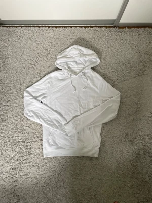 Vit hoodie från Pier One - Säljer en stilren vit hoodie från Pier One. Hoodien har klassisk huva med dragsko och en stor magficka. Tillverkad i mjukt bomullsmaterial som känns skönt mot huden. Perfekt för dig som gillar en clean och enkel look.