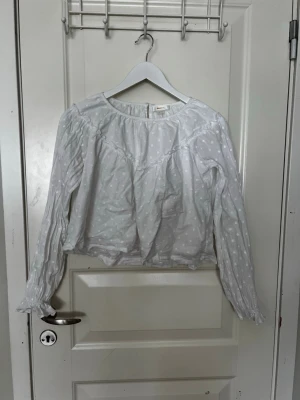 Vit blus med broderade prickar Gina Tricot - Söt vit blus från Gina Tricot med broderade prickar och rund halsringning. Blusen har långa ärmar med resår vid ärmslut och en lös, luftig passform.