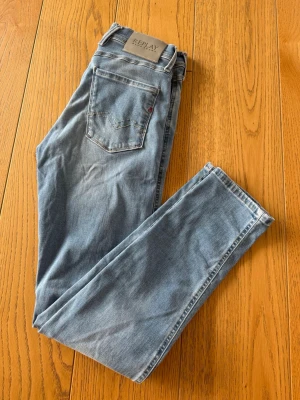 Ljusblå Replay jeans slim fit - Säljer ett par ljusblå jeans från Replay med klassisk femficksdesign och slim fit. Jeansen har snygga slitningar framtill och är tillverkade i mjukt denimtyg som sitter skönt hela dagen. Perfekta till din vardagsstil!