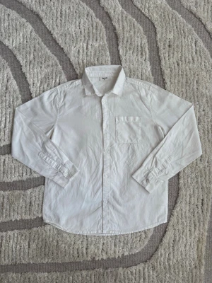 Vit klassisk skjorta med bröstficka - En stilren vit skjorta i bomull med klassisk krage, knäppning framtill och en bröstficka. Skjortan har långa ärmar med manschetter och passar perfekt till både jeans och kostymbyxor.