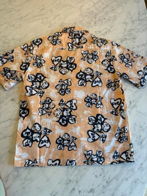 Beige blommig kortärmad skjorta, NN07 - Säljer en beige kortärmad skjorta med svart och vit blommigt mönster. Skjortan har klassisk krage och knappar framtill. Perfekt för dig som vill sticka ut med en unik och färgglad stil. Skjortan är i modell bowlingskjorta. Oanvänd. Nypris 1300 SEK. 