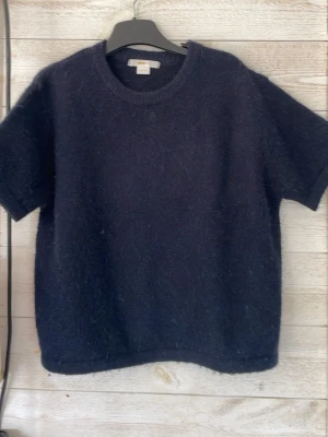 Mörkblå stickad t-shirt - Kortärmad stickad t-shirt i mörkblå färg med rund halsringning. Tröjan har en mjuk, lite luddig yta och en enkel, avslappnad passform. Perfekt för dig som gillar en stilren och mysig look. Den är för liten för mig och skulle vara kul om den kom till användning.💕