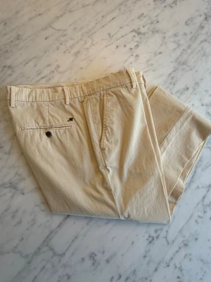 Beige/off white chinos från Masons, smal passform - Snygga beige/oss white chinos från italienska Masons med smal passform och klassiska detaljer som bälteshällor, sidofickor och bakficka med knapp. Tillverkade i ett mjukt bomullstyg som känns skönt mot huden. Perfekta för en clean och stilren look. Oanvända. Nypris 1800 SEK. 