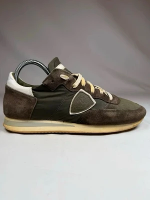 Philippe model sneakers med mockadetaljer - Snygga sneakers i olivgrönt med bruna mockadetaljer och vita inslag. Ovandelen är en mix av mocka och textil, med vita skosnören och en beige sula. Klassisk låg modell med retrovibbar och diskret logga på sidan. Passar 41-42