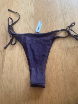 Lila bikiniunderdel med knyt - Snygg lila bikiniunderdel med knyt i sidorna. Modellen har en hög skärning och är perfekt för sommardagar på stranden eller vid poolen. Materialet är mjukt och följsamt för en bekväm passform.