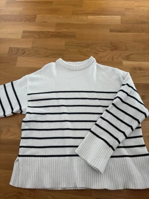 Vit stickad tröja med svarta ränder  - Vit stickad tröja från Lager 157 med svarta horisontella ränder och bred ribbstickad nederkant. Tröjan har rund halsringning och långa ärmar med ribbade muddar. Perfekt för en chill och stilren look.