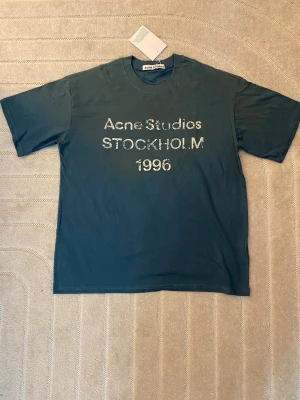 Mörkblå Acne Studios t-shirt M - Snygg mörblå t-shirt från Acne Studios med tryck 'Acne Studios STOCKHOLM 1996' i vitt framtill. Klassisk passform med rund hals och korta ärmar. Perfekt för dig som gillar stilrena plagg med en twist.