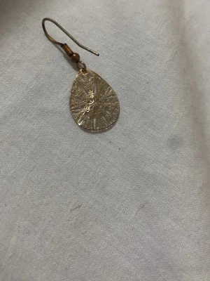Guldigt droppformat örhänge - Snyggt örhänge i droppformad design med ett detaljerat, utskuret mönster. Örhänget är i guldfärgad metall och har en krok för enkel användning. Perfekt för dig som gillar unika accessoarer med lite boho-vibe.