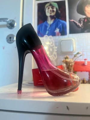 Parfymflaska formad som högklackad sko - Unik parfymflaska i form av en högklackad sko. Flaskan är genomskinlig med rosa och röd toning och har en svart häl och klack. Perfekt som dekoration eller för dig som gillar snygga parfymflaskor med cool design.