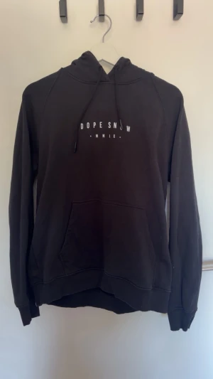 Svart hoodie Dope Snow med tryck - Säljer en svart hoodie från Dope Snow med vitt tryck framtill och stort grafiskt motiv på ryggen med berg och måne. Hoodien har huva med dragsko och en stor magficka. Perfekt för dig som gillar streetwear och snygga detaljer. Använd enbart 1 gång. 
