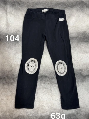 Svarta leggings med virkade knädetaljer - Säljer ett par svarta leggings med elastisk midja och unika vita virkade applikationer på knäna. Perfekta för dig som vill ha något extra till din outfit. 🌸 Fint använt skick. Storlek 104