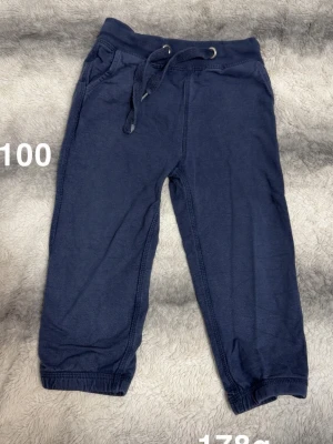 Mörkblå mjukisbyxor med dragsko - Mörkblå mjukisbyxor med resår i midjan och justerbar dragsko. Byxorna har två sidofickor och ribbade muddar vid bensluten. Perfekta för chill dagar eller när du vill vara bekväm. 🌸 fint använt skick. Storlek 100
