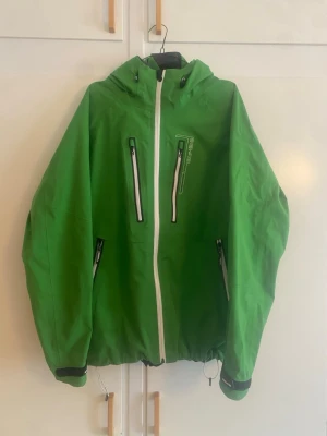8848 Altitude grön skaljacka, Gore-Tex-teknologi - Snygg grön vindjacka med vit dragkedja och svarta detaljer. Jackan har två bröstfickor med dragkedja, två sidofickor och justerbar nederkant med dragsko. Perfekt för blåsiga dagar och outdoor-aktiviteter. Jackan har en sportig look och huva.