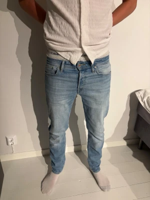 Ljusblå slim fit jeans från Jack & Jones herr - Säljer ett par ljusblå slim fit jeans med klassisk femficksdesign och normal midja. Jeansen har en snygg tvättad look och raka ben. Passar perfekt till en avslappnad stil och är gjorda i mjukt denimtyg.