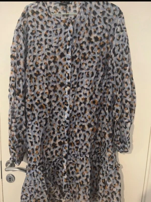 Leopardmönstrad långklänning Lindex - Säljer en långklänning från Lindex med leopardmönster i blå, svart och beige toner. Klänningen har långa ärmar med resår vid handlederna och knappar framtill. Perfekt för dig som gillar djurmönstrat och vill ha en skön och luftig stil.