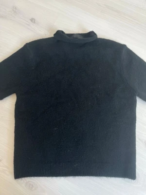 Svart stickad tröja från Zara - Mysig svart stickad tröja från Zara med hög krage och rak passform. Tröjan har korta ärmar och är tillverkad i ett mjukt, fluffigt material som känns skönt mot huden. Perfekt för kyliga dagar och enkel att matcha med olika outfits.