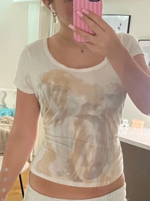 Vit t-shirt med abstrakt tryck från Lee - Säljer en vit t-shirt från Lee med ett stort abstrakt tryck i beige, brunt och grått på framsidan. T-shirten har rund halsringning och korta ärmar. Materialet ser ut att vara mjukt och tunt, perfekt för en avslappnad stil.
